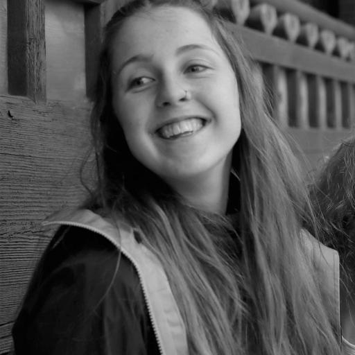 Vera Jung - A white woman with dark blond hair and wearing a a marina blue jacket. Her head is tilted and she is wearing a nose ring. 